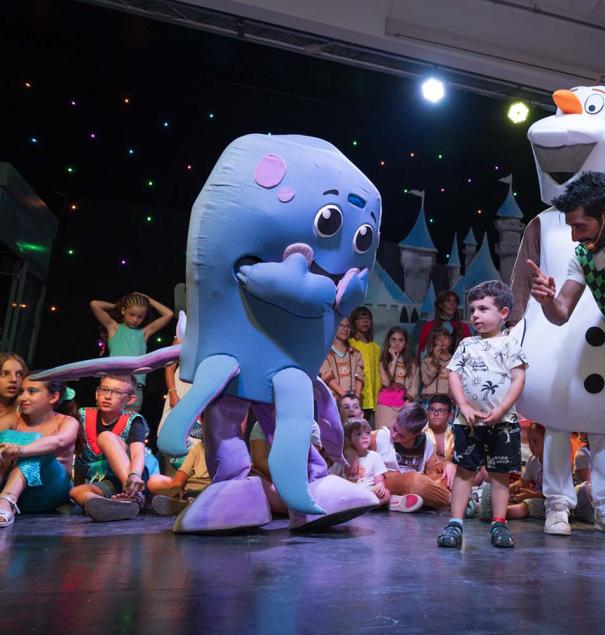 Bambini con personaggi in costume su un palco durante uno spettacolo.