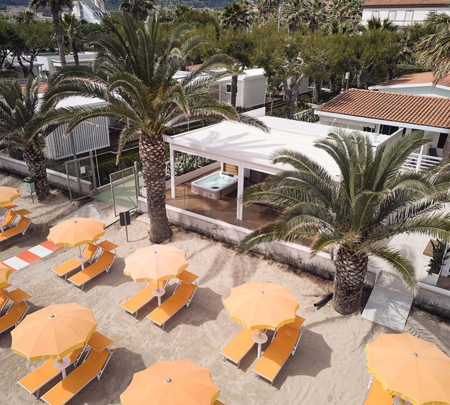 Strand met oranje parasols en palmbomen bij een terras.